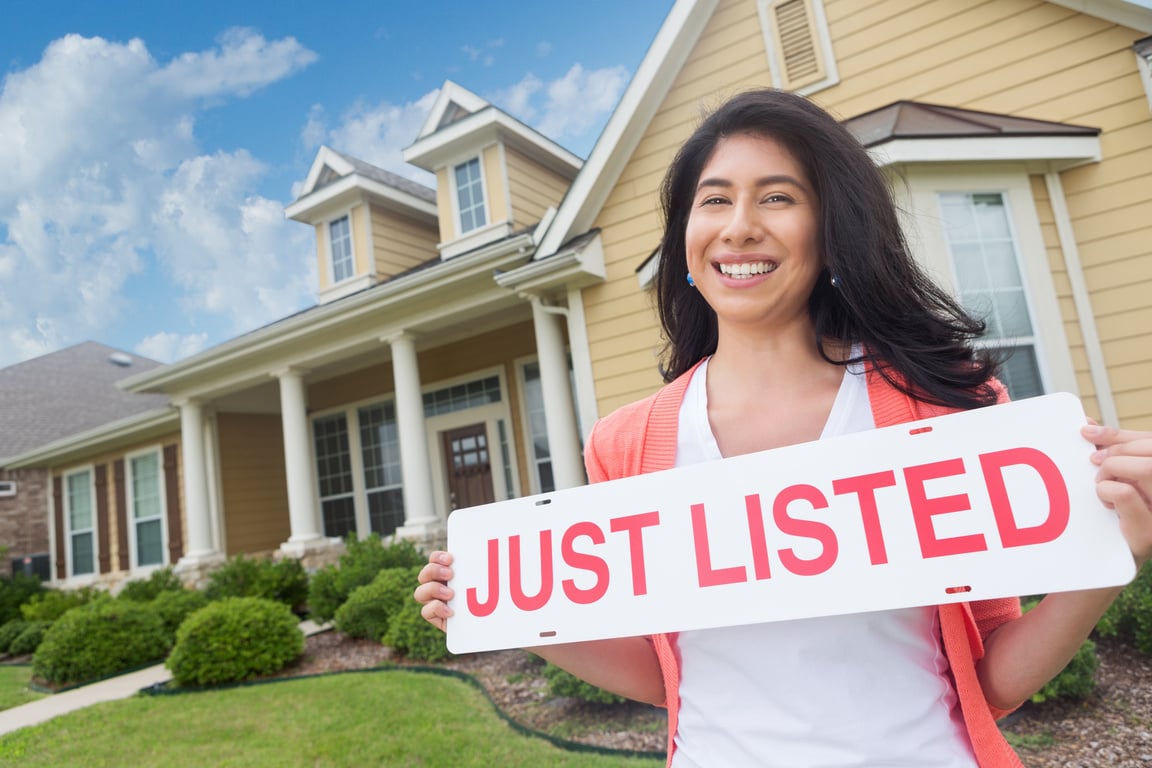 Real estate agent holding 'just listed' sign by house